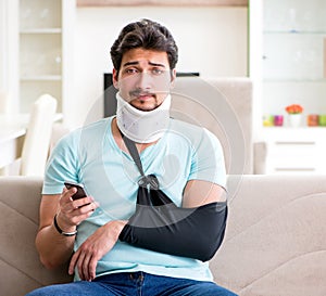 Young student man with neck and hand injury sitting on the sofa