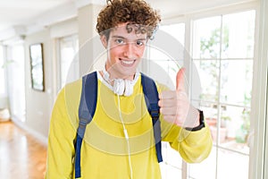 Young student man wearing headphones and backpack doing happy thumbs up gesture with hand