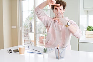 Young student man writing on notebook and studying smiling making frame with hands and fingers with happy face