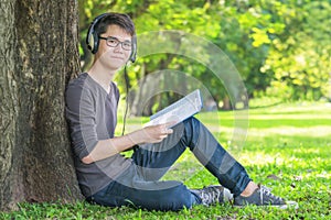 Young student in park listening to music on headphones