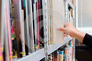 Young student picking a book from the shelf in the library. Preparing for exams, young man searching for or choosing a book in the