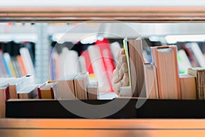 Young student picking a book from the shelf in the library. Preparing for exams, young man searching for or choosing a book in the