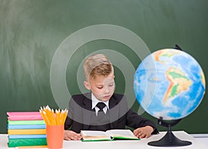 Young student reading a book near empty green chalkboard