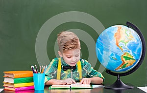 Young student reading a book near empty green chalkboard