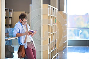 Young student reading book while standing by railing at corridor in university