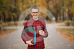 Young student in red checkered shirt with cap of coffee. Portrait of handsome young man holding folders