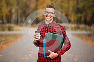 Young student in red checkered shirt with cap of coffee. Portrait of handsome young man holding folders