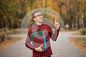 Young student in red checkered shirt point top. Portrait of handsome young man holding folders