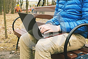 Young student sitting on bench with laptop in park