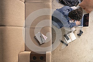 Young student sitting on the floor of his classroom doing his homework, he is connecting to the internet with a laptop