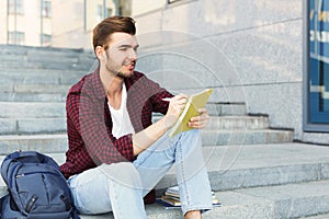 Young student making notes sitting on stairs