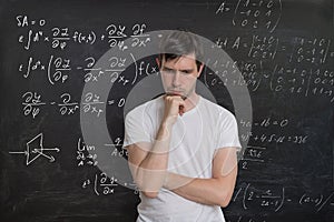 Young student is solving math exam. Mathematics formular on blackboard in background