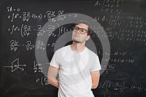 Young student is solving math exam. Mathematics formular on blackboard in background