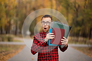Young student with surprised face looks out of folder in red checkered shirt. Portrait of handsome young man
