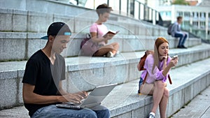 Young student typing laptop sitting campus stairs, digital generation, freelance