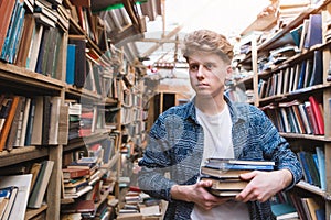 Young student walking in a library with books in his hands and looking for literature