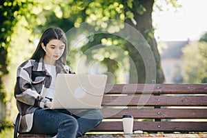 Young student watching lesson online and studying from park. Woman college university student using laptop computer