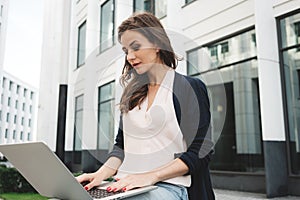 Young student woman sits in city park with modern laptop