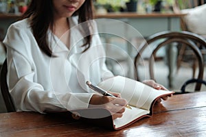 Young student woman sitting at library holding pen and writing o