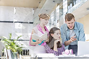 Young students discussing over laptop while making assignment at table in university