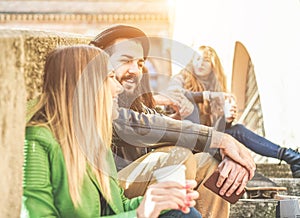 Young students drinking coffee in paper ripley cup outdoor during a university break - Cheerful friends toasting cappuccino in old