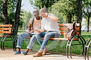 Young students sitting on bench and studying in park together