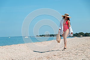 young stunning woman in red swimsuit walking by sea beach