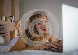 Young stylish attractive and beautiful Caucasian woman 30s lying on bed at night in home bedroom using internet at laptop computer