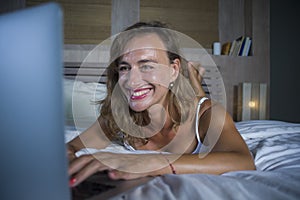 Young stylish attractive and beautiful Caucasian woman 30s lying on bed at night in home bedroom using internet at laptop computer