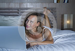 Young stylish attractive and beautiful Caucasian woman 30s lying on bed at night in home bedroom using internet at laptop computer