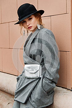 Young stylish beautiful woman fashion model is posing in street, wearing pantsuit, having purse on her waist