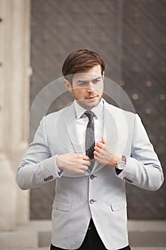 Young stylish businessman adjusting his suit, neck tie