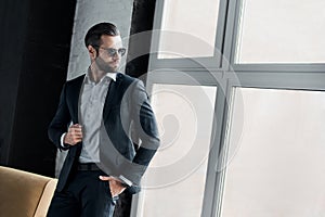 Young stylish businessman leader indoors at office wearing sunglasses looking out the window