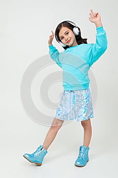 Young stylish charming girl in a turquoise blouse and boots enjoys music on headphones and dances in a studio with white