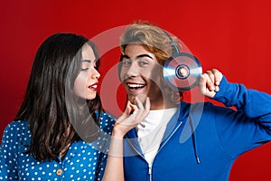 Young stylish couple in blue clothes showing music CD standing on the red background