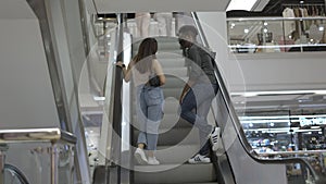 Young stylish couple riding an escalator in the mall as they speak. Couple goes shopping together