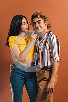 Young stylish couple wearing colorful clothes standing on the orange background