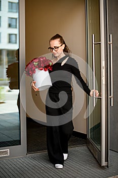 Young stylish dark hair girl accurate holds in hands big round box with large red peony flowers.