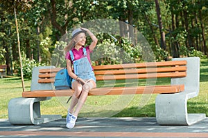 Young stylish dressed girl sitting on the bench keeping a book.