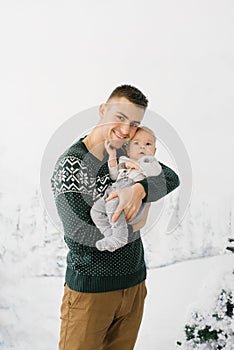 Young stylish father and little son on winter vacation in winter holiday photo zone. The father holds his son in his arms