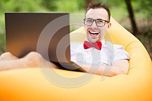 Young stylish freelancer man in glasses working at laptop sitting on Inflatable mattress in garden. Online education