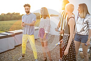 Young stylish friends celebrating on the rooftop at sunset