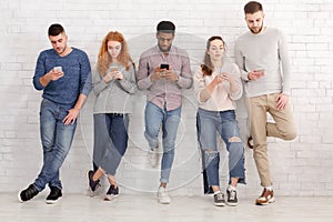 Young stylish friends using devices over brick wall