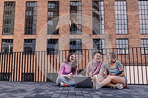 Young stylish generation Z students sitting in front of school building.