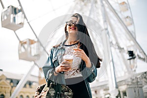 Young stylish girl enjoys summer and vacation. Brunette in trendy sunglasses walks in the city