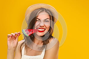 Young stylish girl in a straw hat with a lollipop on a yellow background. Summer concept with copy space. Girl bites off candy