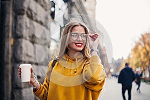 Young stylish girl student wearing bright yellow sweatshirt.Close-up portrait of inspired young woman laughing and touching glasse