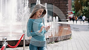 Young, stylish girl uses a smartphone on a city street, a woman prints a message, chatting