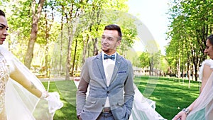 Young stylish groom looking pleased at three sexy brides walking around his