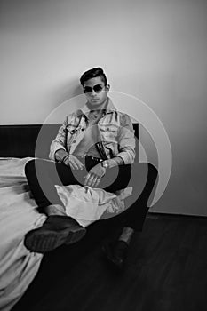 Young stylish guy in denim jacket on the bed. black and white photo with fine grain effect. selective focus